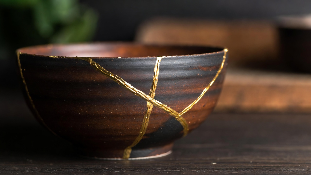 Handcrafted Kintsugi bowl with gold cracks on a dark wooden background, representing resilience and the beauty of imperfection.